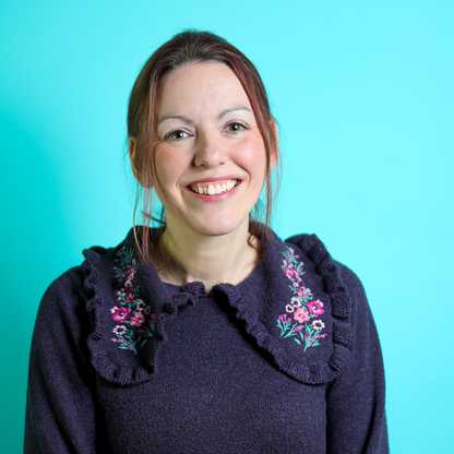 "Person in a dark blue embroidered sweater against a turquoise background, face blurred."