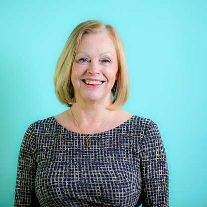 "Person with shoulder-length blonde hair in a patterned dress, face blurred, against turquoise background."