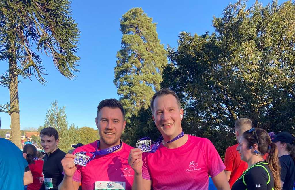 Two men in claire house running tops and medals in their hands after finishing a run at Alton towers