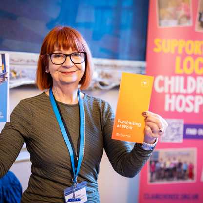 Person holding two hospice fundraising pamphlets in front of a banner promoting local children's hospice support.