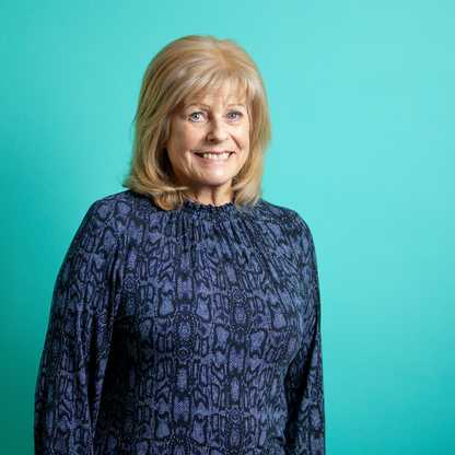 "Person in a dark blue patterned top, face blurred, against turquoise background."