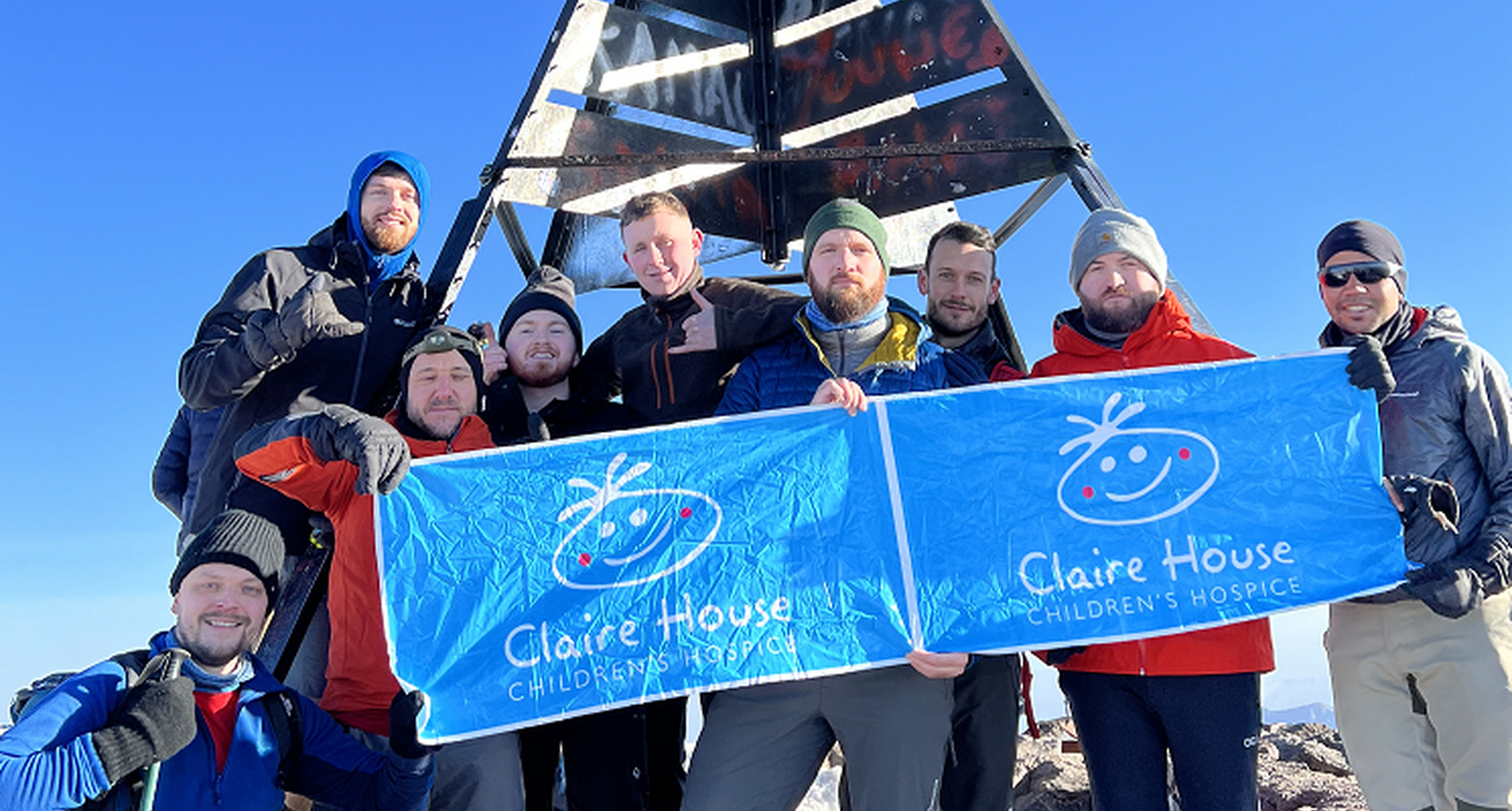 nine people after completing a trek holding a claire house banner