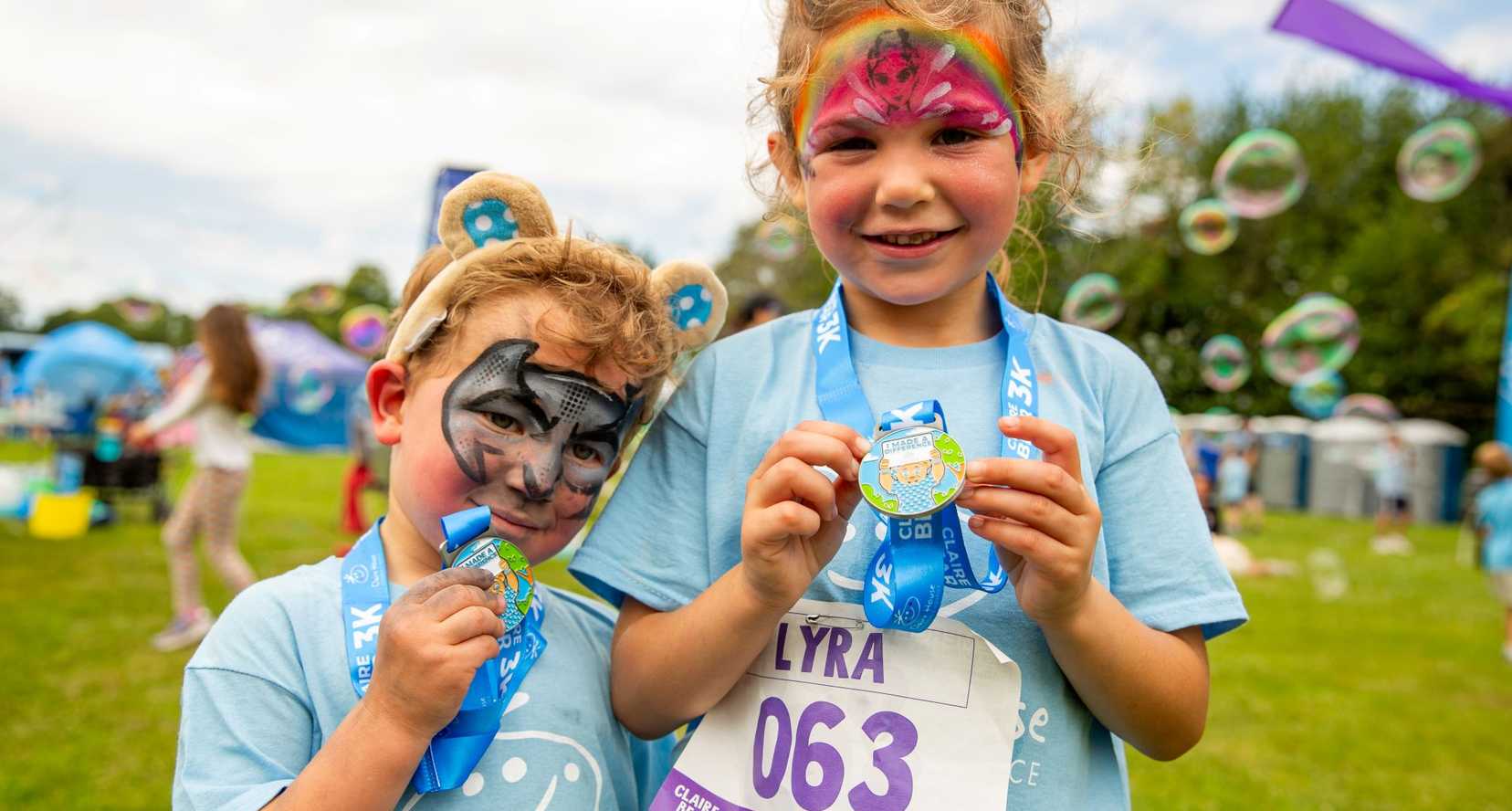 Young girls with their faces painted showing off their Claire Bear 3K medals